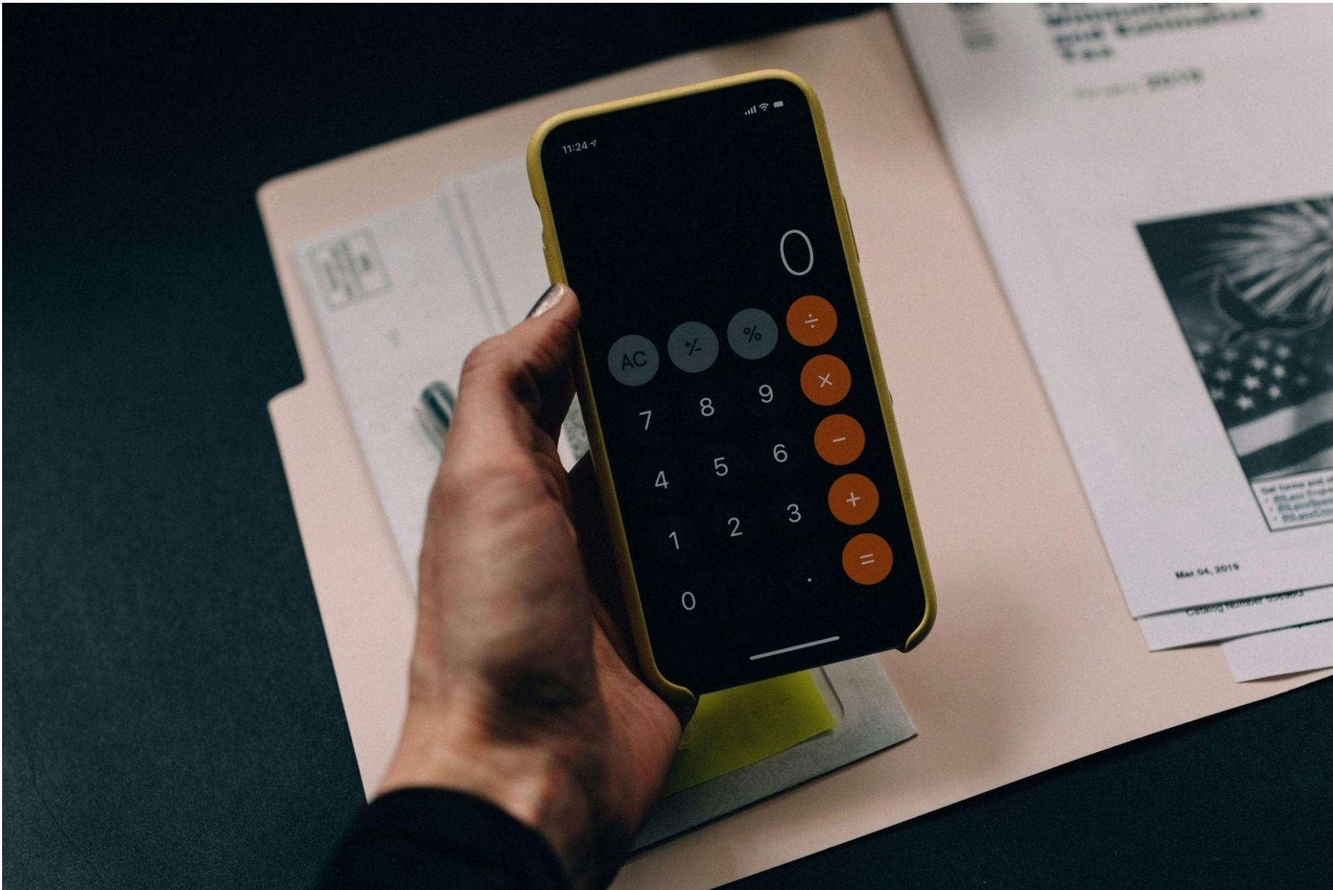 A hand holding a smartphone with a calculator app open over budgeting documents