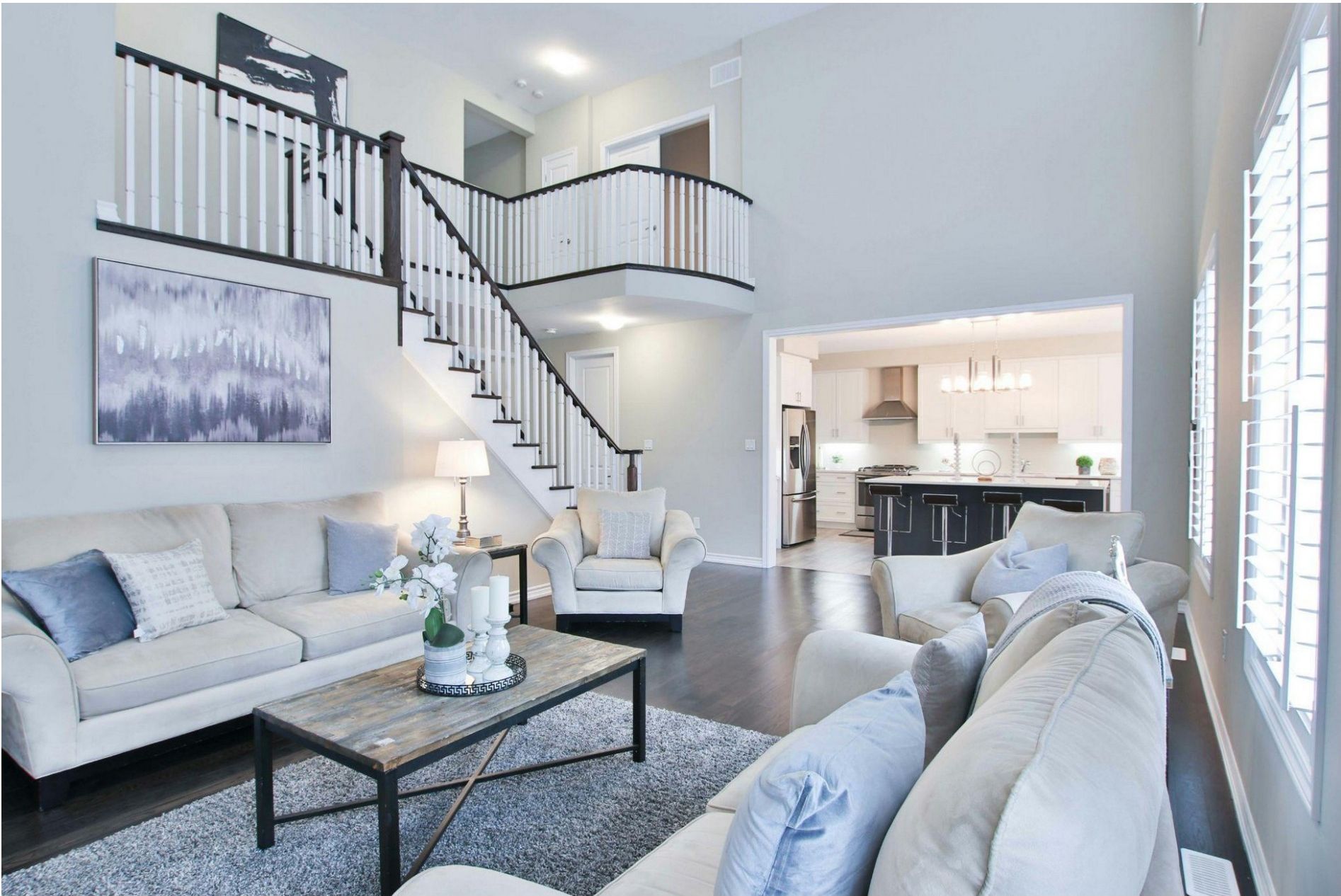 A modern living room with a staircase leading to an upper level and a view into the kitchen